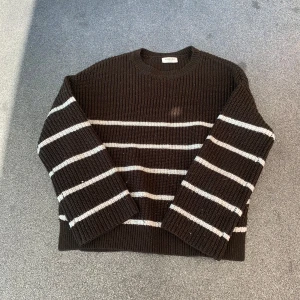 Randig stickad tröja från Kappahl - Mysig stickad tröja från Kappahl i mörkbrunt med vita horisontella ränder. Tröjan har en klassisk rund halsringning och långa ärmar. Perfekt för lager-på-lager och chill dagar. Ribbstickad struktur ger en skön och avslappnad vibe.
