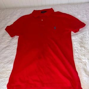 Röd Polo Ralph Lauren t-shirt slim fit - Riktigt snygg röd t-shirt från Polo Ralph Lauren i slim fit-modell. Klassisk pikékrage med två knappar och den ikoniska blå broderade loggan på bröstet. Nypris: Ca 1599, Mitt pris:349. Självklart äkta
