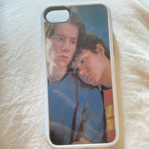 Mobilskal med young royals-tryck - Säljer ett mobilskal med coolt young royals-motiv i färgerna blå, röd och gul. Skalet har vit ram och svart insida med bikakemönster för extra grepp. 