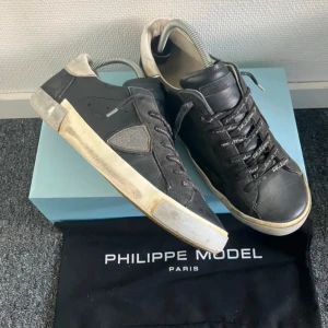 Svarta Philippe Model sneakers i skinn - Snygga svarta sneakers från Philippe Model Paris med detaljer i beige och vit. Skorna har snörning med logotyp på skosnörena, rund tå och platt sula. Ovandelen är i skinn och mocka, med Philippe Model-märke på hälen och sidan. Dustbag och box 