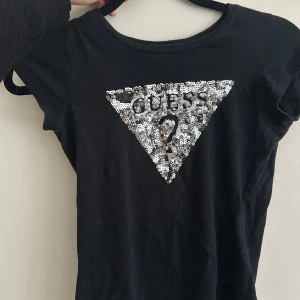 Svart topp med paljetter från Guess - Supercool t-shirt från Guess! Alla paljetter är kvar och den rä i 100% bomull. Säljer då den är för liten för mig! 🪩🪩🪩🪩