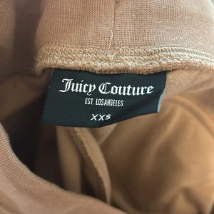 Pris kan absolut diskuteras! Beige velourbyxor Juicy Couture XXS - Byxorna är lite uppsydda men inte mycket alls. Jag har väldigt långa ben och dom är ungefär 4 cm för korta.Supermjuka beige velourbyxor från Juicy Couture i storlek XXS. Byxorna har bred resår i midjan, snörning med metalldetaljer och fickor med knappar bak. Klassisk JC-logga broderad framtill. Perfekta för en chill och trendig look.