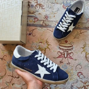 Blå Golden Goose sneakers med vit stjärna - Snygga sneakers från Golden Goose i mörkblå mocka med vit stjärndetalj på sidan och vit häl. Skorna har vita snören och platt sula. Perfekta för dig som gillar en sportig och trendig look med premiumkänsla.