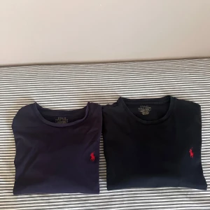 2-pack Polo Ralph Lauren t-shirts - Två klassiska t-shirts från Polo Ralph Lauren i marinblått och svart, båda med röd broderad logga på bröstet. T-shirtsen har rund hals, kort ärm och är gjorda i mjuk bomull. Perfekta för en clean och stilren look. Köpte båda för 1200 för några månader sedan. Storlek S På Båda T-shirten. Pris kan diskuteras vid snabb affär! 😴😊