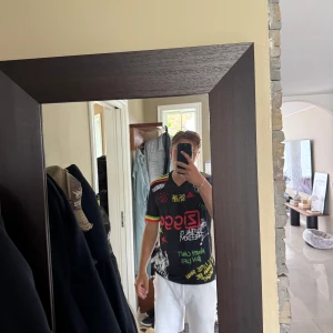 Ajax x Bob Marley svart t-shirt - Säljer en svart Ajax x Bob Marley t-shirt från Adidas med färgglada tryck och graffiti-inspirerade texter. Riktigt go tröja med fin kvalité 