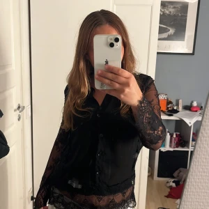 Svart spetsblus från Amisu XS - Supersnygg svart blus från Amisu i transparent spets med knappar framtill. Långa ärmar i spets och fina spetsdetaljer längs nederkant och ärmslut. Perfekt för dig som vill sticka ut lite extra med en elegant vibe. Super fin, hanterad väl. Knappt använd 💕 Pris kan diskuteras 