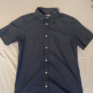 Svart kortärmad skjorta Jack & Jones - Svart skjorta från Jack & Jones i klassisk modell med korta ärmar och knappar framtill. Skjortan har en stilren krage. Perfekt för dig som gillar enkel och clean stil.