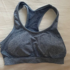 Grå sportig linnetopp med meshdetaljer - Säljer en blå sportig linnetopp med snygga meshpaneler på sidorna och ryggen för extra ventilation. Toppen har brottarrygg och är tillverkad i ett stretchigt syntetmaterial som passar perfekt till träning. Enkel och stilren design som ger en cool vibe.