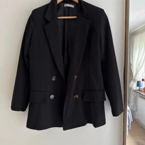 Svart kavaj Made in Italy - Stilren svart kavaj med dubbelknäppning och klassisk krage. Kavajen har två fickor framtill med lock och snygga knappar i guldton. Står att den är i storlek 10 (M) men skulle säga att den är mer åt S 