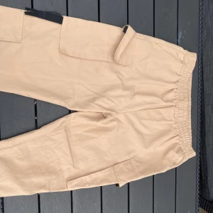 Beiga cargopants med resårmidja - Säljer ett par beiga cargopants med resår i midjan som ger en skön fit, och stora fickor på sidorna. Byxorna har en avslappnad passform och är tillverkade i ett mjukt bomullstyg. Perfekta för en chill och streetig stil.