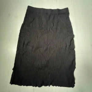 Svart ribbad långkjol  - Säljer en svart långkjol från KappAhl i ribbat material. Kjolen har en elastisk midja och lätt vågig nederkant, vilket ger en snygg och avslappnad look. Perfekt att styla med en stickad tröja och bälte för en trendig outfit.