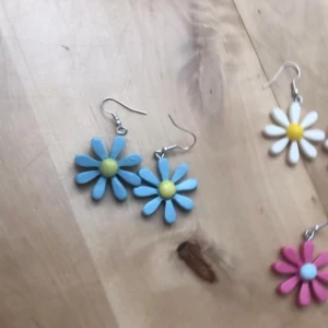 Färgglada blommiga örhängen - Säljer flera par örhängen i form av stora blommor i olika färger: blå med gul mitt, vita med gul mitt, rosa med ljusblå mitt och gula med vit mitt. Perfekta för dig som vill sticka ut med ett lekfullt och färgstarkt smycke. Krokar i metall och priset gäller för ett par örhängen. Jag har ett par av alla örhängen förutom de vita med gul mitt (2 par) och de gula med vit mitt (2 par)💞