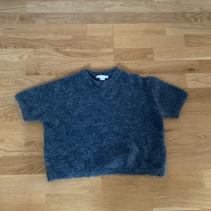 Grå stickad tröja från Gina Tricot - Mysig grå stickad tröja från Gina Tricot med korta ärmar och boxig passform. Perfekt för lager-på-lager och chill dagar. Tröjan har en enkel design utan mönster och är superenkel att matcha med jeans eller kjol.