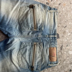 Ljusblå jeans med dragkedjor - Säljer ett par jättecoola ljusblå bootcut jeans med slitna detaljer och coola dragkedjor på bakfickorna. Midjemått: 36cm rakt över, Innerbenslängd: 85cm, Grenmått: 18 cm🫶Skriv privat för fler bilder! 