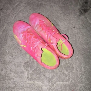 Nike Zoom rosa fotbollsskor - Säljer ett par Nike Zoom fotbollsskor i en riktigt snygg rosa färg med gula detaljer och sula. Skorna har snörning och är tillverkade i syntetmaterial för lätt känsla på planen. Perfekta för dig som vill sticka ut på matchen!