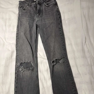 Grå flared jeans med hål - Säljer ett par grå jeans från Gina med flared modell med snygga slitningar och hål vid knäna. Jeansen har medelhög midja och råa kanter nertill. Sitter riktigt snyggt! 