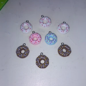 Donut-berlocker i olika färger - Söta donut-berlocker i vitt, rosa, blått och brunt med färgglada strössel. Perfekta att använda som hängen till halsband eller armband. De har en rund form och små öglor för att enkelt fästa på smycken. Supergulliga och unika detaljer till din stil!