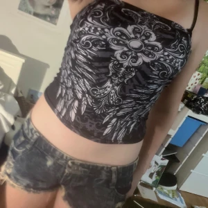 Y2k grunge tubtopp - Säljer en svart bandeau tubtopp med fett tribalinspirerat mönster i vitt och grått. Toppen är croppad och sitter tight, perfekt för dig som gillar edgy och alternativ stil. Materialet känns mjukt och stretchigt, och toppen är ärmlös med axelbandslös design. 