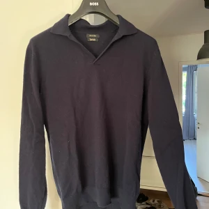 Mörkblå ulltröja från Massimo Dutti - Snygg mörkblå långärmad tröja från Massimo Dutti i mjuk ullmix. Tröjan har klassisk krage med v-ringning och ribbade muddar. Perfekt för dig som gillar stilrena och tidlösa plagg med en clean look.