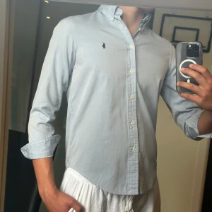 Ljusblå skjorta från Ralph Lauren - • Nu säljs en ljus blå Ralph lauren skjorta i mycket bra skick 👔 • Storleken är 16 år och han på bilden är ca 177cm 📏 • Mycket snygg och fräsch skjorta nu till sommaren. Den är dessutom skön då den har ett avslappnat material ⭐️ • Nypris på denna är ca 1600kr men säljs för ett ofattbart bra pris på snåla 319kr ! • Det kan förekomma små fläckar men inget som märks av vid användning 🫟 • Hör av dig vid minsta lilla fundering 🤔💭 • Kolla gärna in profilen för andra schyssta plagg som raffe skjortor, l