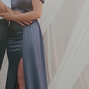 Mörkblå långklänning med slits - Säljer en elegant mörkblå långklänning i satin material. Klänningen har korta ärmar, markerad midja och en hög slits framtill som ger en snygg och modern look. Perfekt för fest, bröllopet som vill sticka ut med stilren och sofistikerad vibe. Passar xs-s