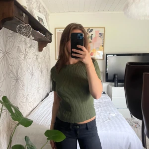 Olivgrön ribbad topp med kort ärm - Snygg olivgrön ribbad topp med korta ärmar och croppad passform. Toppen har rund halsringning och är stickad i ett mjukt material som sitter skönt på kroppen. Perfekt att styla med jeans eller kjol för en trendig look.