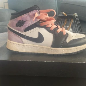 Nike Air Jordan 1 Mid i svart, vit & lila - Nike Air Jordan 1 Mid sneakers med svart och vit läderbas, lila textilpaneler och rosa snören. Klassisk svart swoosh och Air Jordan-logga på sidan. Skorna har rund tå, snörning och en platt sula. Perfekt för dig som vill sticka ut med en unik färgkombo.                                                                    Ny pris gick på runt 1100 kr, säljer för 150 kr! Kvaliteten är riktigt bra på skon men skick är ganska bra, ge dem bara lite skrubb så ser dem riktigt feta ut. Kontakta gärna!
