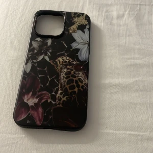 Mobilskal med leopard och blommor - Snyggt mobilskal med mörk bakgrund, leopardmönster och stora blommor i vitt och vinrött. Skalet har även detaljer som ett guldigt smycke och körsbär. Perfekt för dig som vill ha ett unikt och trendigt mobilskal.