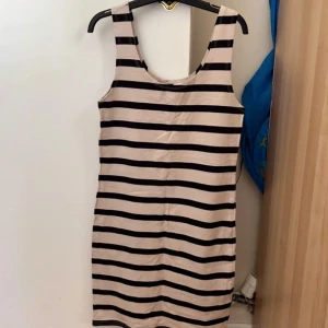 Randig kortklänning från H&M Divided - Snygg ärmlös kortklänning från H&M Divided i beige och svart med breda horisontella ränder. Klänningen har en rund halsringning och är tillverkad i mjuk bomull, perfekt för en chill och stilren look.