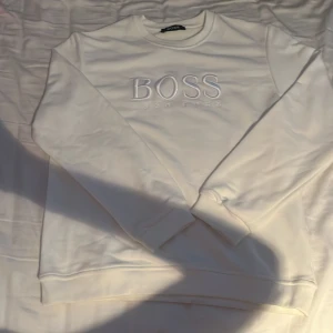Vit sweatshirt från Hugo Boss - Snygg vit sweatshirt från Hugo Boss med broderad logga på bröstet. Tröjan har rund halsringning och långa ärmar, perfekt för en clean och stilren look. Tillverkad i mjuk bomull för maximal komfort.