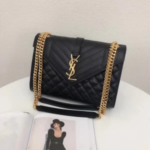 Svart quiltad axelväska från Saint Laurent - Säljer en svart quiltad axelväska från Saint Laurent med ikoniskt YSL-emblem i guld framtill. Väskan har kedjerem i guldmetall och är tillverkad i präglat skinn. Klassisk och stilren design med lock och magnetlås, perfekt för att lyfta vilken outfit som helst.