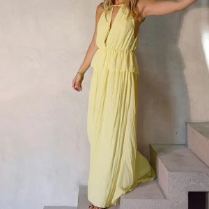 Ljusgul långklänning med v-ringning - Helt ny, oanvänd (prislapp kvar). Superfin ljusgul långklänning med djup v-ringning och ärmlös design. Klänningen har ett flowy fall och markerad midja med volangdetalj. Perfekt för sommarens alla tillfällen när du vill känna dig extra chic.