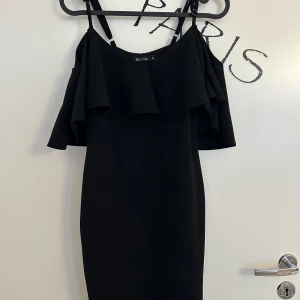 Svart volangklänning från NLY One - Supersnygg svart kortklänning med volangdetaljer över axlarna och smala axelband från NLY One i storlek S. Klänningen har en figurnära passform. Klänningen är i mycket bra skick. 