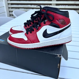 Nike Air Jordan 1 Chicago sneakers - Ikoniska Nike Air Jordan 1 Chicago sneakers i rött, vitt och svart skinn. Klassisk high-top siluett med svart swoosh, svarta snören och perforerad tå. Perfekta för dig som vill sticka ut med en tidlös streetwear-look.