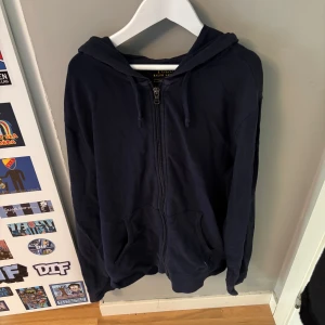 Mörkblå hoodie från Polo Ralph Lauren - Säljer en mörkblå hoodie från Polo Ralph Lauren med dragkedja och huva. Tröjan har långa ärmar, känguruficka och den klassiska broderade loggan i vitt på fickan. Tillverkad i mjuk bomull, perfekt för chill dagar.