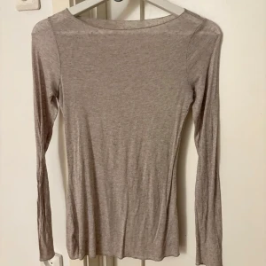 Beige långärmad tunn tröja - Superskön och tunn långärmad tröja i beige nyans. Tröjan har en enkel, stilren design med rund halsringning och smal passform. Perfekt att ha som lager eller för en clean look. Materialet känns mjukt och följsamt mot huden.