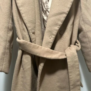 Beige kappa med bälte från H&M - Snygg beige kappa från H&M i storlek 42. Kappan har klassisk krage, knappar framtill och ett matchande bälte i midjan. Utsidan är mjuk och insidan har ett lent foder. Perfekt för dig som vill ha en stilren och tidlös look. Den var köpt för 1000kr så jag säljer den då för halva priset men ändå så går det att diskutera priset och sänka!🩷🙌
