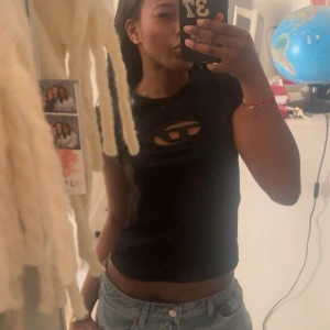 Svart croppad diesel topp med cut-out - Säljer en svart croppad diesel topp med cool cut-out detalj över bröstet och korta ärmar. Perfekt för dig som vill sticka ut med en edgy vibe. Passar snyggt till jeans eller kjol.