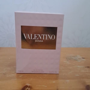 Valentino Donna Eau de Parfum 100ml - Lyxig parfym från Valentino i en elegant, diamantmönstrad glasflaska med guldiga detaljer och lock. Doften kommer i en ljusrosa kartong med guldfärgad etikett. Flaskan rymmer 100 ml och utstrålar exklusivitet och stil.