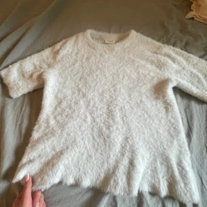 Vit fluffig stickad tröja - Supermjuk och fluffig vit stickad tröja. Tröjan har rund halsringning och halv-långa ärmar, perfekt för dig som gillar en cozy och trendig vibe. Passar till både jeans och kjol för en chill look.