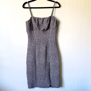 Blommig långklänning från H&M Divided - Supersöt långklänning med smala axelband från H&M Divided. Klänningen har ett blommigt mönster i svart, rosa och vitt, figurnära passform och en snygg slits framtill. Perfekt för sommarens alla tillfällen!