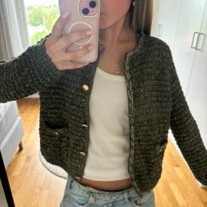 Grön stickad cardigan jacka från mango  - Säljer en grön stickad cardigan jacka från Mango med guldiga detaljer. Jackan har knappar framtill, två fickor och en mysig, chunky känsla. Perfekt att slänga över en t-shirt för en chill och snygg look.