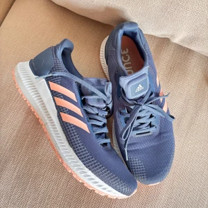 Adidas Solar Blaze sneakers blå/korall - Snygga Adidas sneakers i blå mesh med korallfärgade detaljer och sula. Skorna har klassiska tre ränder på sidan, snörning och en bekväm, dämpad sula perfekt för träning eller långa promenader.