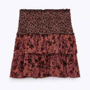 Blommig volangkjol i brunrosa - Supersöt kort kjol med volanger och blommigt mönster i brunrosa toner. Smockad midja för skön passform och flowig känsla. Perfekt för dig som gillar romantisk och trendig stil.