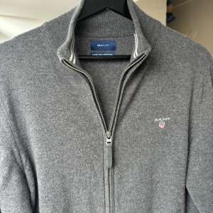 Grå half-zip i lammull från Gant - Säljer en snygg grå kofta från Gant i lammull. Perfekt för lager-på-lager och passar till allt. Klassisk och stilren look. Säljer pga den blvit för liten. Köpt på NK för 1100kr