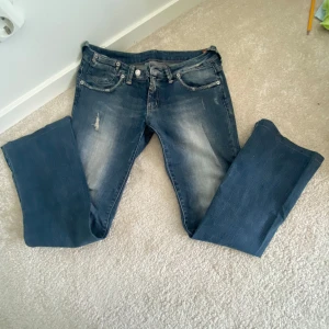 Blå bootcut jeans med slitningar - Snygga blå lågmidjadd jeans med bootcut passform och slitna detaljer på låren. Stor i storleken. 