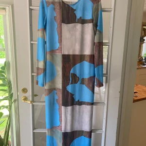Meshklänning från Monki, storlek M - Unik långklänning från Monki med coolt abstrakt mönster i blått, brunt och grått. Klänningen har lång ärm och figurnära passform. Materialet är stretchigt och tunt, perfekt för dig som gillar statement-plagg med konstnärlig vibe. Storlek medium