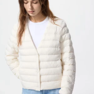 Beige dunjacka från Uniqlo - Säljer en stilren, beige  dunjacka från Uniqlo med rund halsringning och horisontella sömmar. Jackan är lätt, har lång ärm och stängs med knappar framtill. Perfekt att slänga på sig när det är kyligt ute.