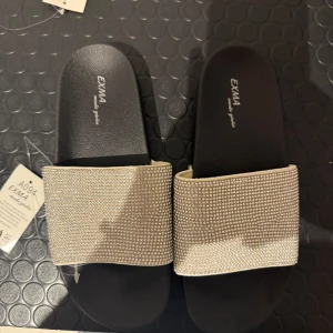 Svarta sandaler med glittriga detaljer - Svarta sandaler från EXMA med bred rem täckt av glittrande stenar. Helt oanvända inget fel på tofflorna, vill bara inte ha dem