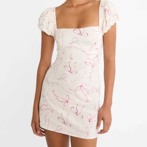 Vit kortklänning med rosa rosettprint stradivarius  - Supersöt vit kortklänning med puffärmar och fyrkantig urringning. Klänningen har ett rosa rosettprint över hela tyget och sitter figurnära. Perfekt för sommarens alla tillfällen och ger en riktigt gullig vibe.